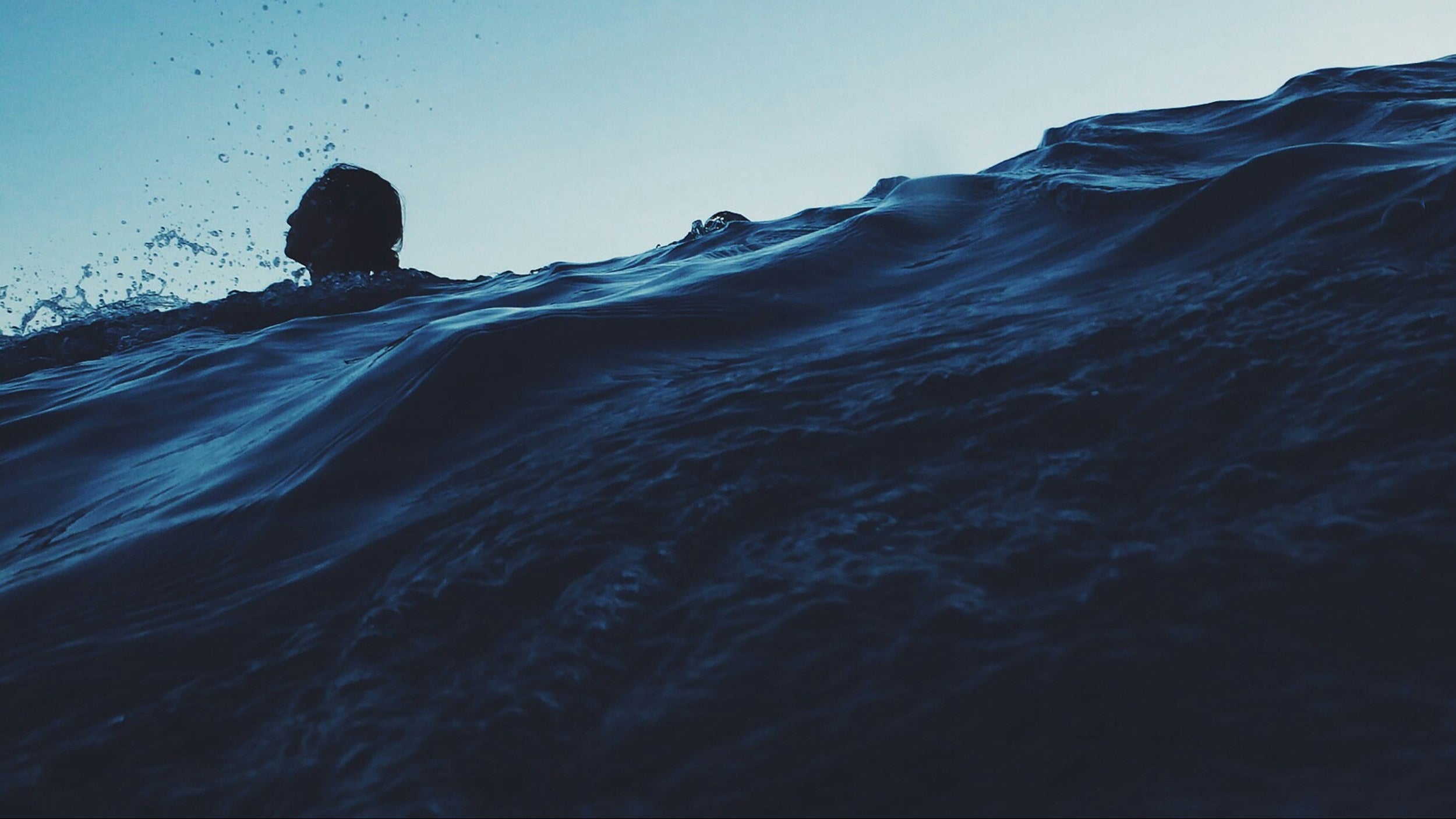 Person swimming underwate with a clear blue sky above